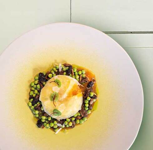 Potato ravioli filled with soft egg yolk and ricotta on a pea and morel ragout Image